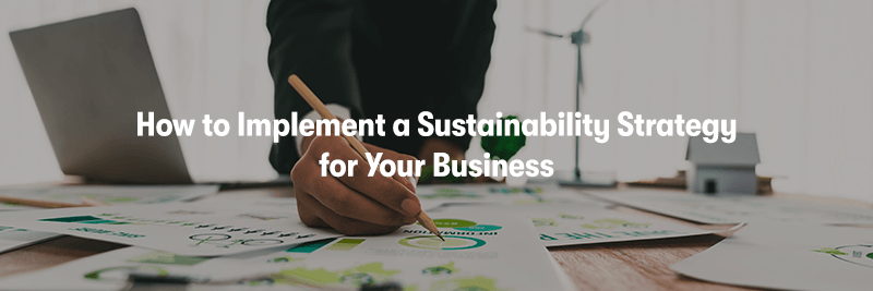 A picture of a man working on sustainability at a desk with lots of pieces of paper on it, with a laptop. With the heading 'How to Implement a Sustainability Strategy for Your Business' in front.