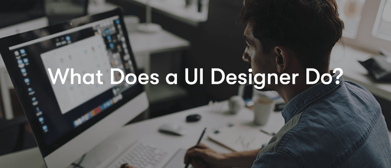 What Does a UI Designer Do? text in front of a man sat at a desk working on his computer