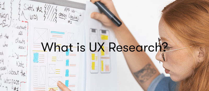 a woman looking at a board with UX research on it and designs, with the words what is UX research on top