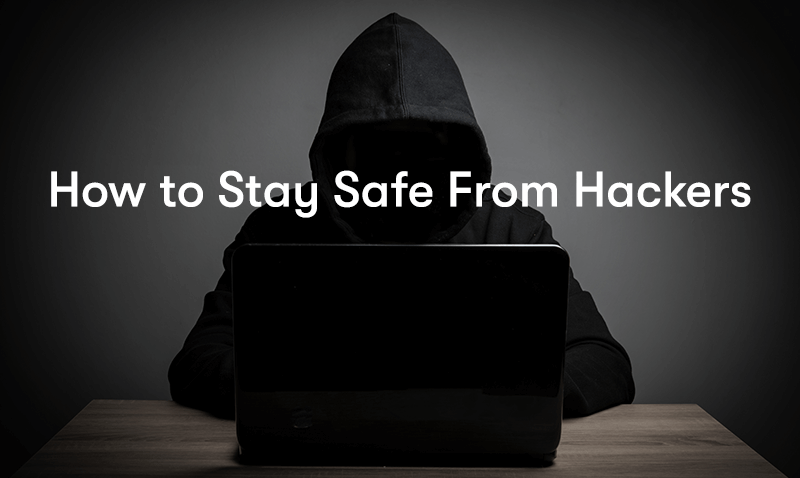 a hacker sat at a desk with a laptop in a dark hoodie hiding their face, with the words How to Stay Safe From Hackers in front