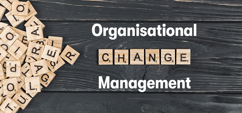 A picture of a pile of scrabble tiles on the left. With the scrabble tiles on the right spelling change, with the word Organisational above and management below. To spell organisational change management. On a dark wood background.